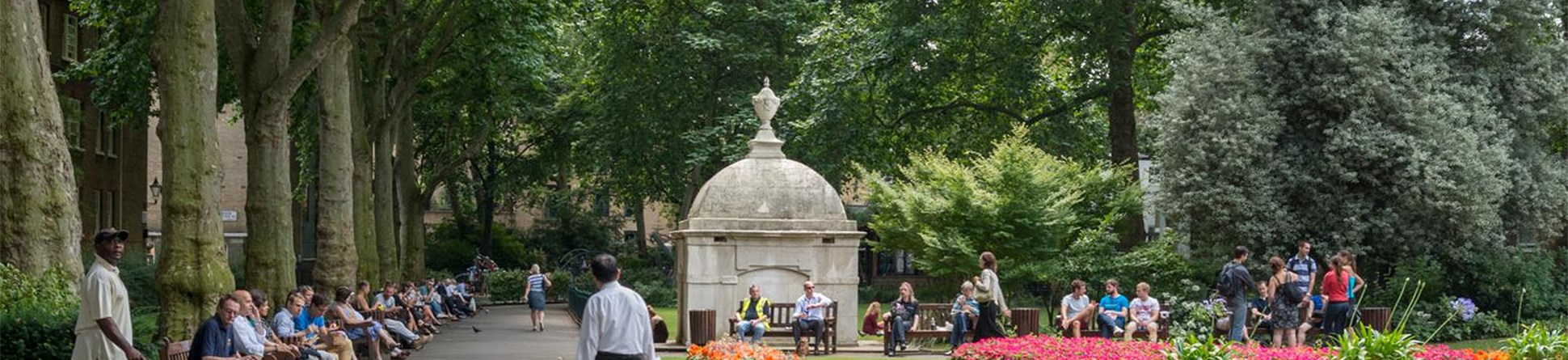 People seated on benches around flower beds in a park with a mausoleum in the background