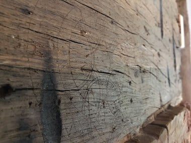 Small daisy wheel scribed on to the wooden surface over an inglenook fireplace