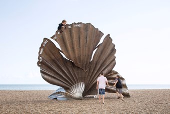 Children climbing on a scallop sculpture on a beach