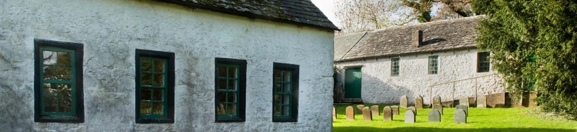 Exterior shot of Pardshaw meeting house with white walls and green window frames in a burial ground.