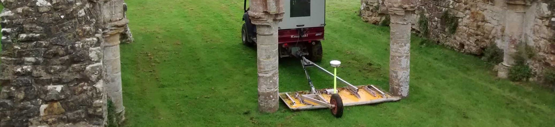 A vehicle towing geophysical survey equipment  passing through an arch within medieval ruins.