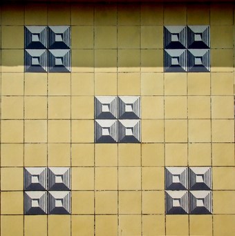 Detail view showing a small section of tiles. The decorative pattern is made up of groups of black & white geometrically patterned tiles set amidst a background of square yellow tiles.