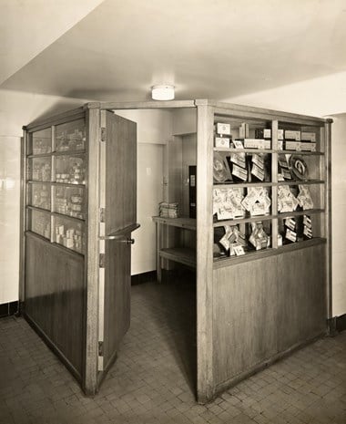 A timber kiosk constructed in the corner of the Ladies room. The camera is looking directly towards the open door giving access to the shop. Items for sale are displayed in ‘windows’ around the exterior of the kiosk.