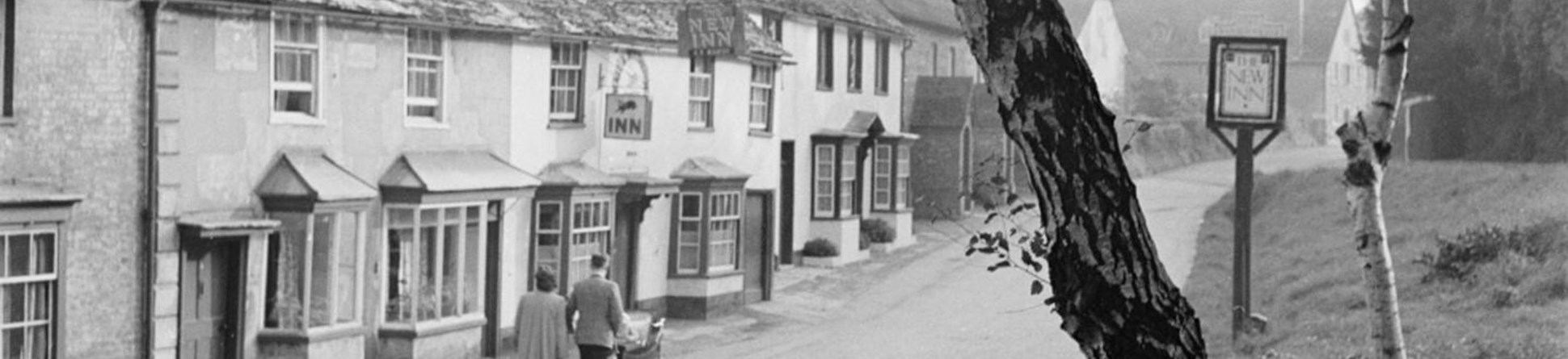 A man and a woman pushing a pram along Dorchester Hill and past the New Inn at Lower Bryanston
