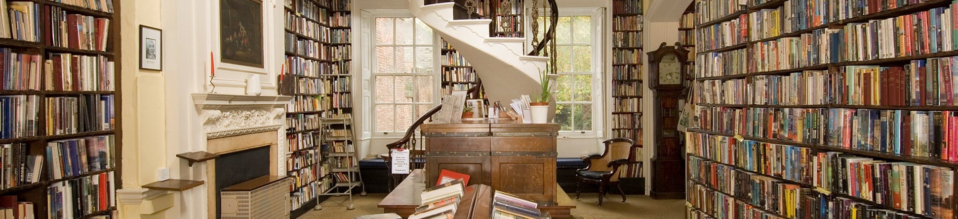 Photo of the inside of Bromley House Library, with shelves filled with books and a spiral staircase at the far end