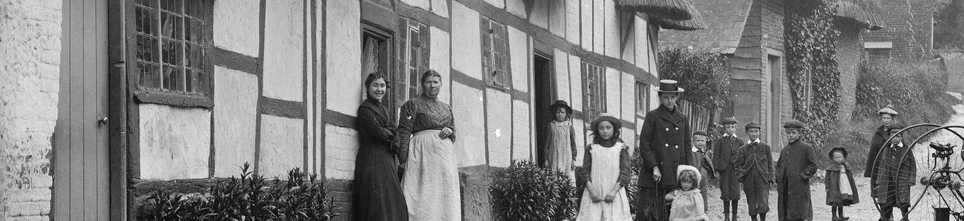 Exterior view of women and children posing outside a thatched cottage