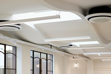 A close-up photograph of an interior ceiling with white bar lights and air ducts