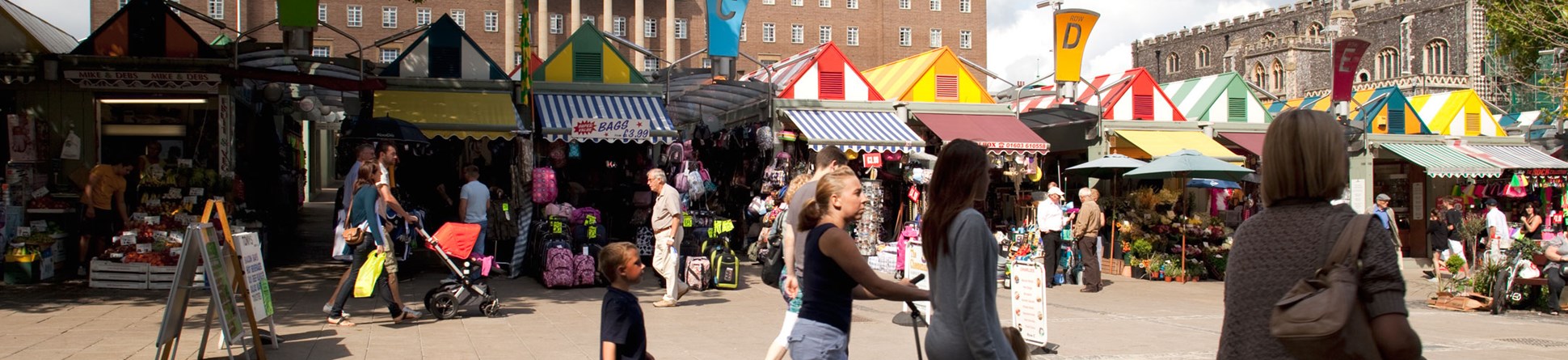 People around market stalls with a large civic building in the background.