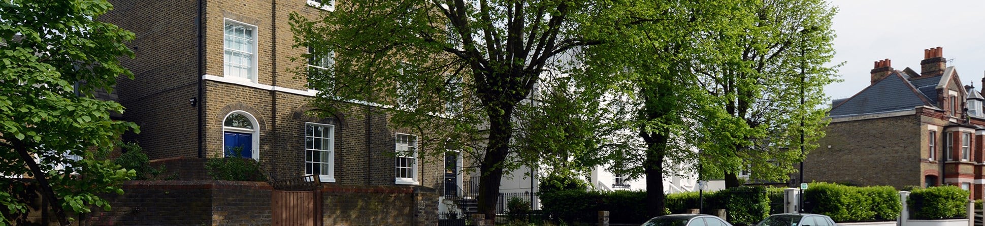 Photo of a Georgian 4 storey terraced house in London (view from the across the street) with a brick wall and large green tree in front