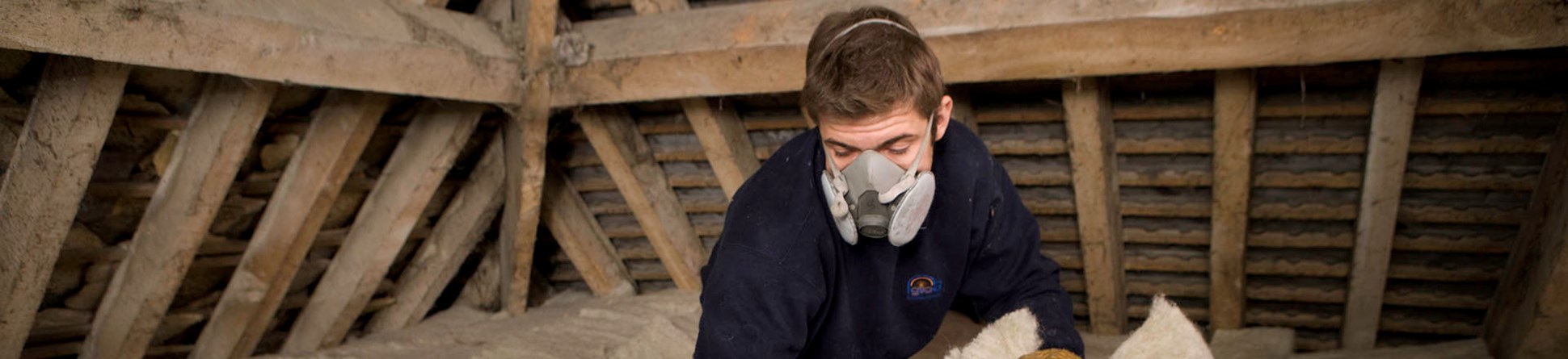 Man wearing mask laying insulation in roof space