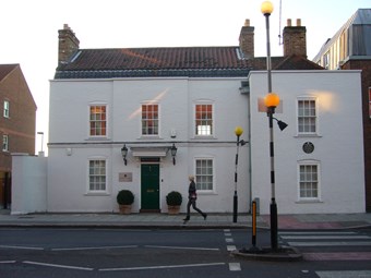 Symmetrical two storey 18th-century house, three windows wide, with additional bay to right. Built of brick, painted white. The central doorway has a doorhood. On the right-hand bay, a green plaque commemorates Cesar Picton. Zebra crossing to right.