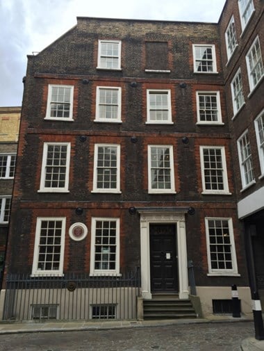 Four-storey red brick town house, four windows wide, with doorway to right. The sash windows painted white. On the ground floor, to left, a brown plaque commemorating Dr Johnson. On the railings in front, a black plaque commemorating Francis Barber