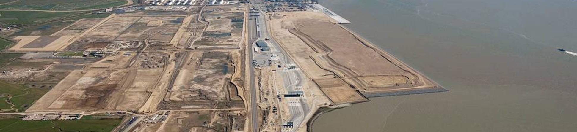 An oblique aerial colour photo of a London Gateway development, to the right is a large silty river, to the left a large industrial area.