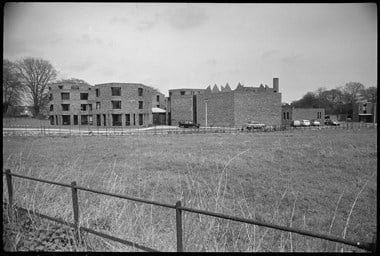 Black and white photo of three-storey hexagonal block building viewed across a field.