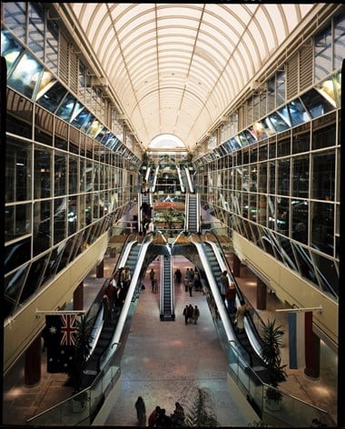 Colour photograph showing the interior of the Eastgate Centre with multiple curved escalators and a vaulted ceiling. Shoppers are walking through the building and riding the escalators.