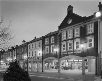 Black and white photograph showing the Scotch Street facade and entrance to The Lanes Shopping Centre, with lights on at night. British Home Stores is on the right of the image.
