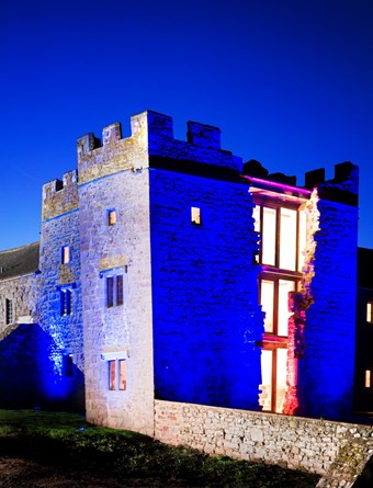 an old building or a castle with brickwork illuminated in blue. Central section shows windows lit up at night.