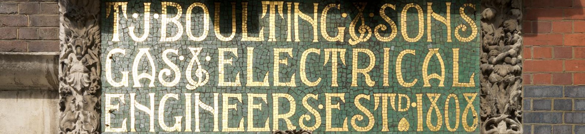 Signage in gold letters with green background. The signage is surrounded by brickwork and other architectural features