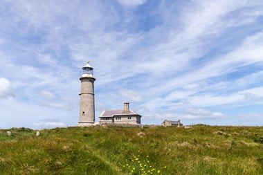 Photo of Lighthouse rising above the horizon above the grass surroundings