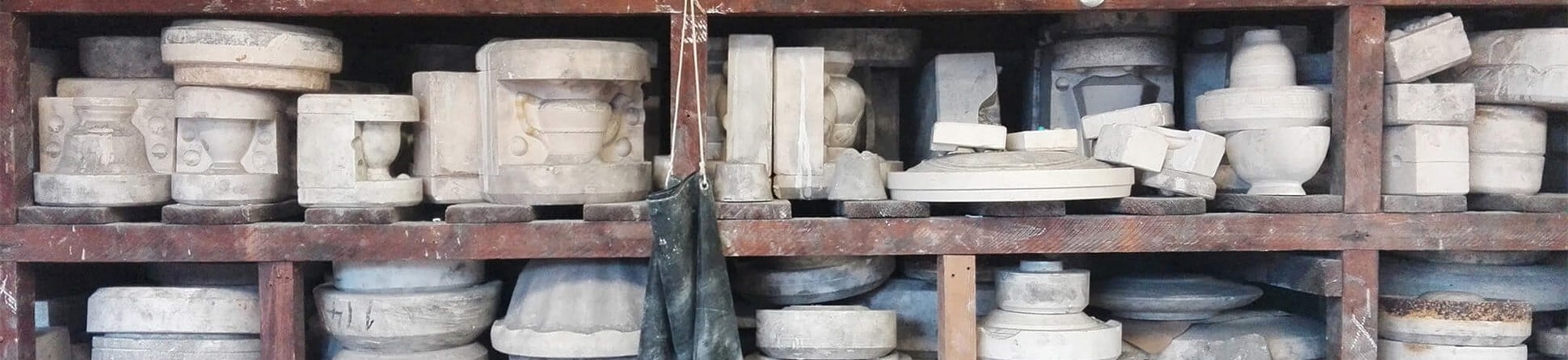 Photograph of shelves in a workshop stacked with plaster moulds for casting tableware ceramics. Varying sizes of moulds for teapots, bowls and cups are on display.