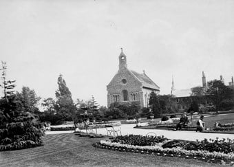 Black and white photo of church with people sitting in a public garden in the foreground