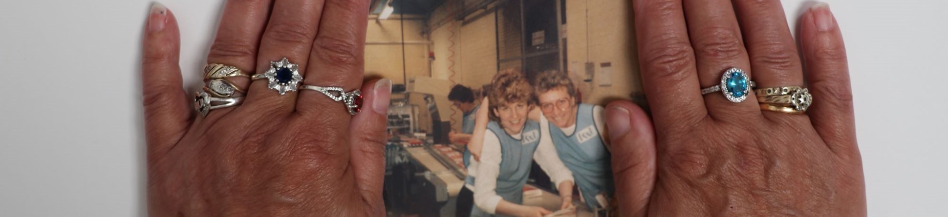 A photo showing hands holding a printed photograph of women at work in the 1980s. 