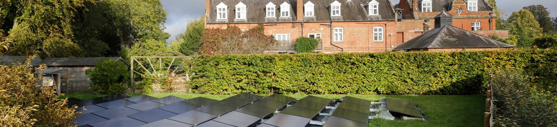 Solar panels surrounded by hedging with a large historic house in the background.