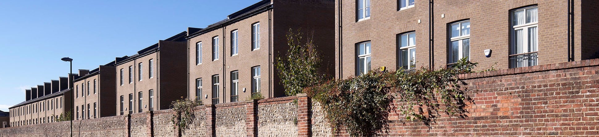 An exterior view of a boundary wall and redeveloped blocks of brick housing.