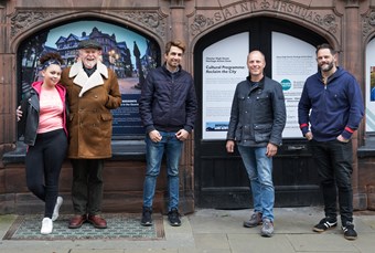 Four men and a woman pose for a photo in front of signage and branding for the Reclaim the City community project.