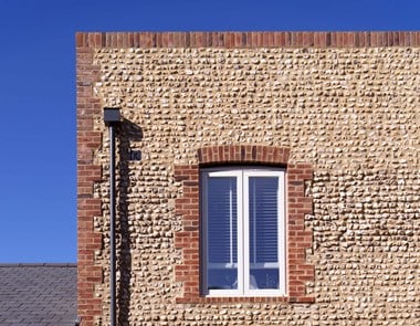 Detail of a modern residential building with flint walling and brick quoins and window details.
