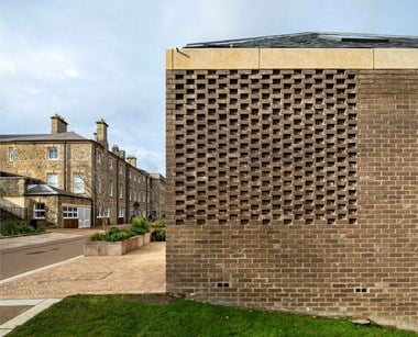 Detail of lattice brickwork to the end wall of a unit of modern mews style housing development at a historic estate, with the older mansion in the background.