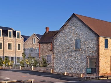 A group of modern dwellings in vernacular styles, with a car park in the foreground.