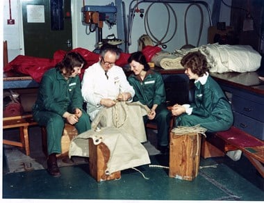 A man repairing a sail loft with three women dressed in overalls looking on