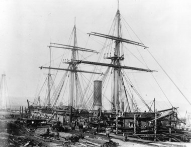 Old photo of a sailing ship in dock with 3 masts and a funnel