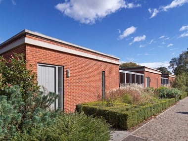 Three single-storey, flat-roofed red brick buildings with associated planting.
