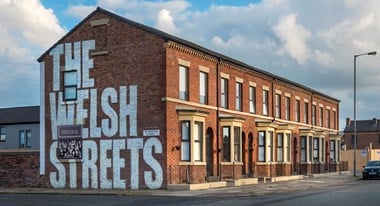 Refurbished Victorian brick terraced housing,  'The Welsh Streets' is painted in large lettering on the near gable end.