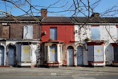 A view of a rundown group of terraced houses with metal shutters over the windows.