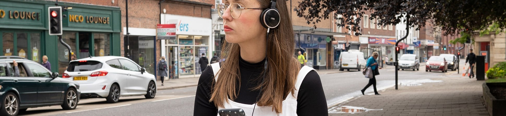 Woman walking down a high street listening to something on headphones.