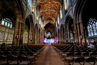 Wide landscape shot of the gothic-looking interior of Chester Cathedral, with a brightly lit nativity scene display at the back of the nave.