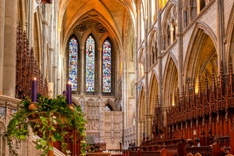 Ornate interior of Truro Cathedral, lit with warm lighting. In the foreground there are three candles nestled among festive foliage.