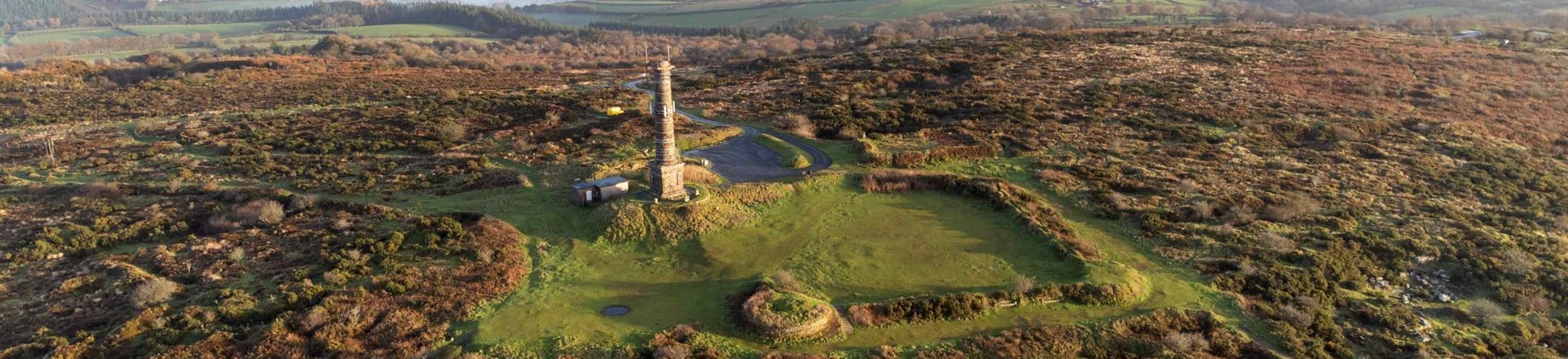 Aerial view from south across the site of Kit Hill, Cornwall. It shows a folly in the centre surrounded by the countryside.