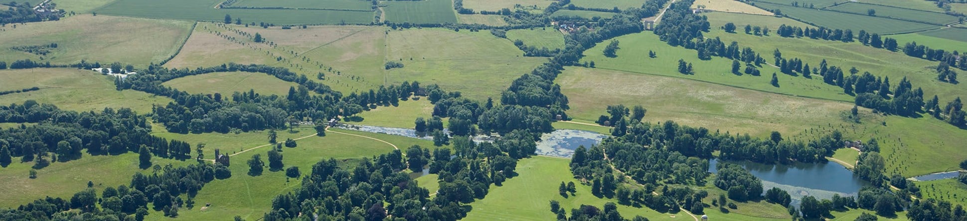 Colour aerial photo showing an ornamental lake surrounded by parkland and trees with arable fields beyond.