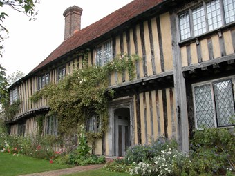 Timber framed house with leaded windows and borders of garden and climbing plants.