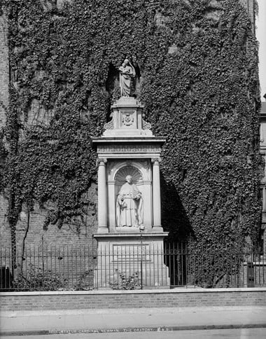 Black and white photo of a white monument next to a building wall covered in ivy