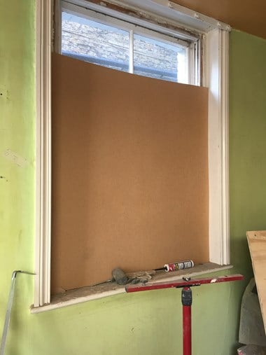 A plywood board covering the bottom three-quarters of a sash window in a green wall.