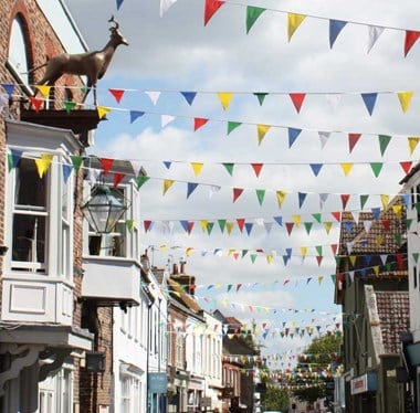 A view down a historic high street with colourful bunting strung between the shops