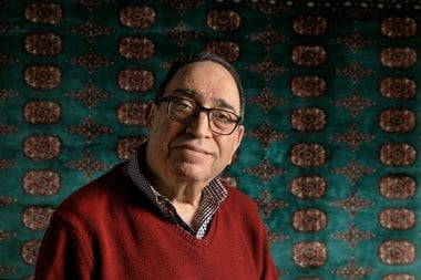 Head and shoulders portrait of a man in front of green oriental carpet.