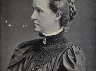 Black and white photo of Millicent Fawcett with hair up in a plaited coil on the back of her head, wearing high collared Edwardian dress. Photo taken approx 1897.