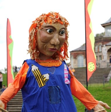 A close-up of a large human puppet within a street scene.