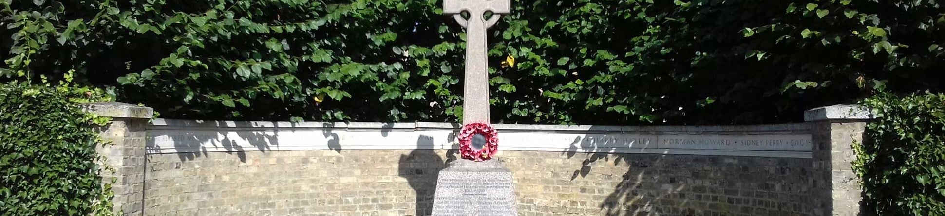 A Celtic cross stands on a tapering plinth in a semi-circular remembrance wall